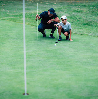 Golf Putting Training. Golf Instructor with Young Boy Practicing on the Putting Green